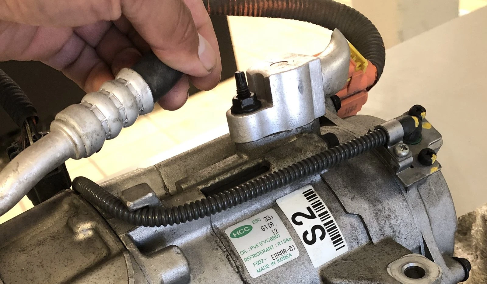 A failed AC compressor off a Hyundai Sonata on the bench at Supercanic in Hemet, with its label showing PVE oil and R134a refrigerant