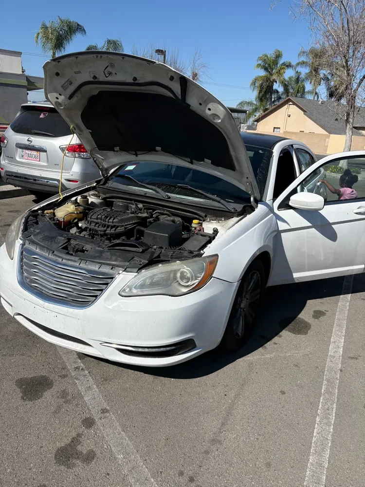 A Chrysler 200 with the hood up in a Hemet driveway, a mobile repair in progress
