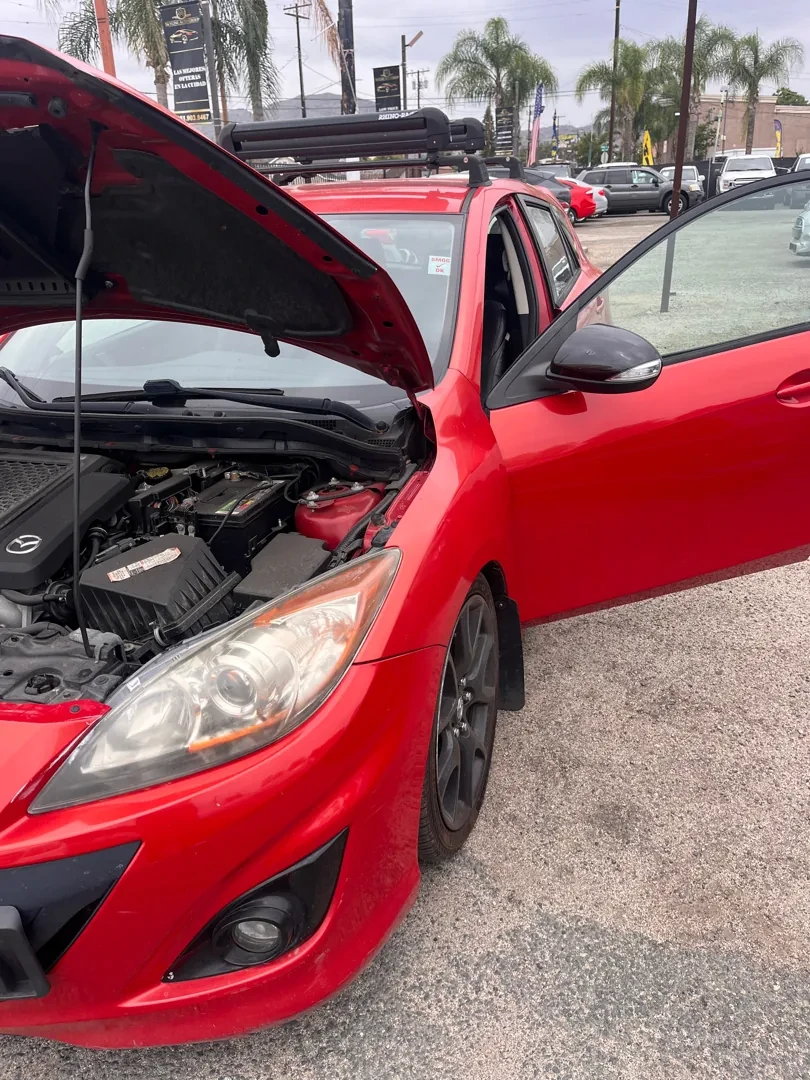 A red Mazda3 with the hood and door open in a Riverside parking lot during a mobile repair