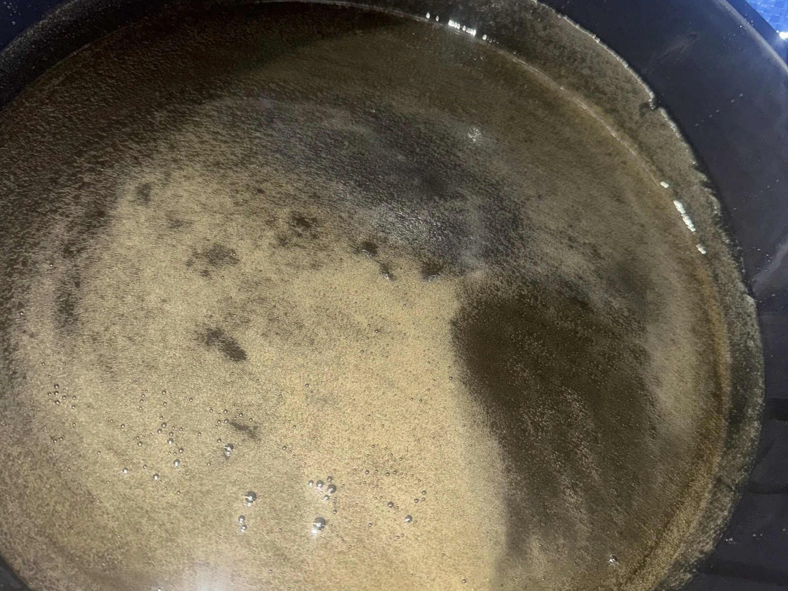 Milky tan engine oil in a black drain pan on a blue tarp at a roadside job