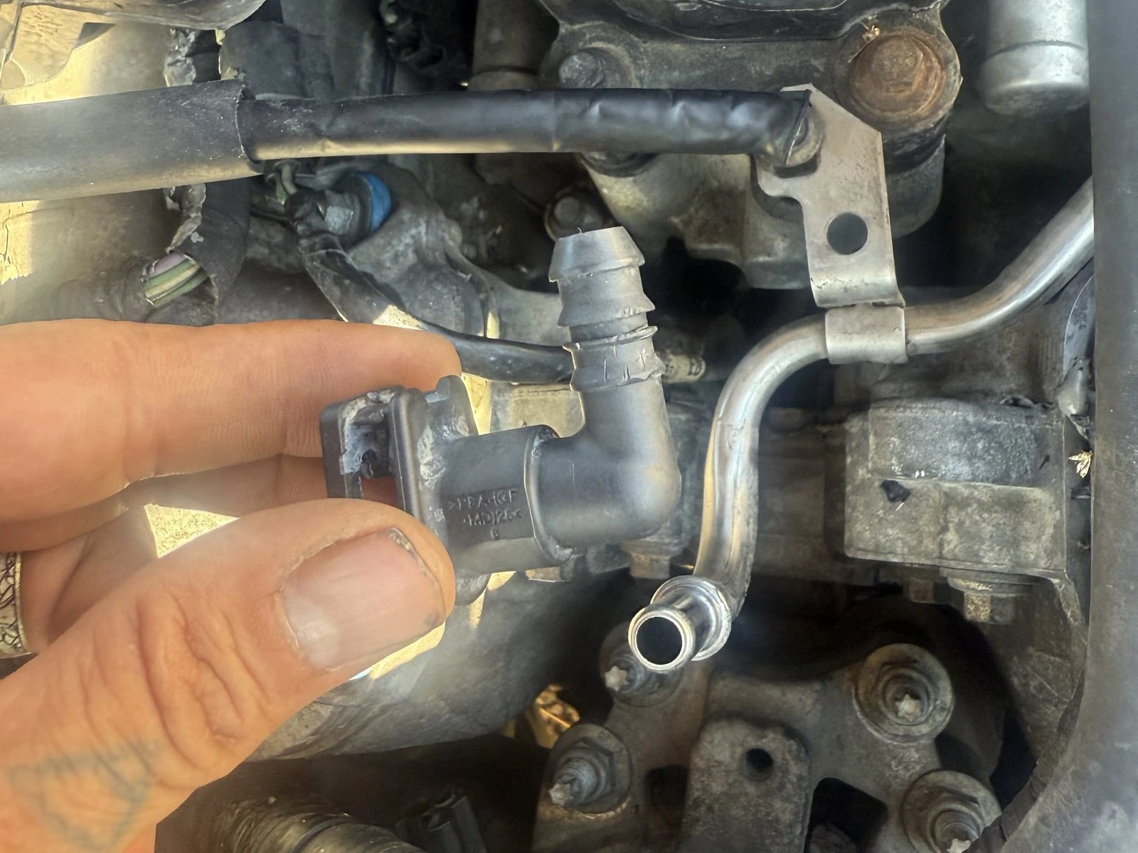 A Supercanic tech holding a brittle gray plastic PCV elbow pulled from under the intake on a Hemet job