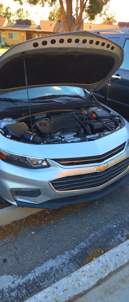 A Chevrolet Malibu with the hood up at the curb on a street call in Jurupa Valley