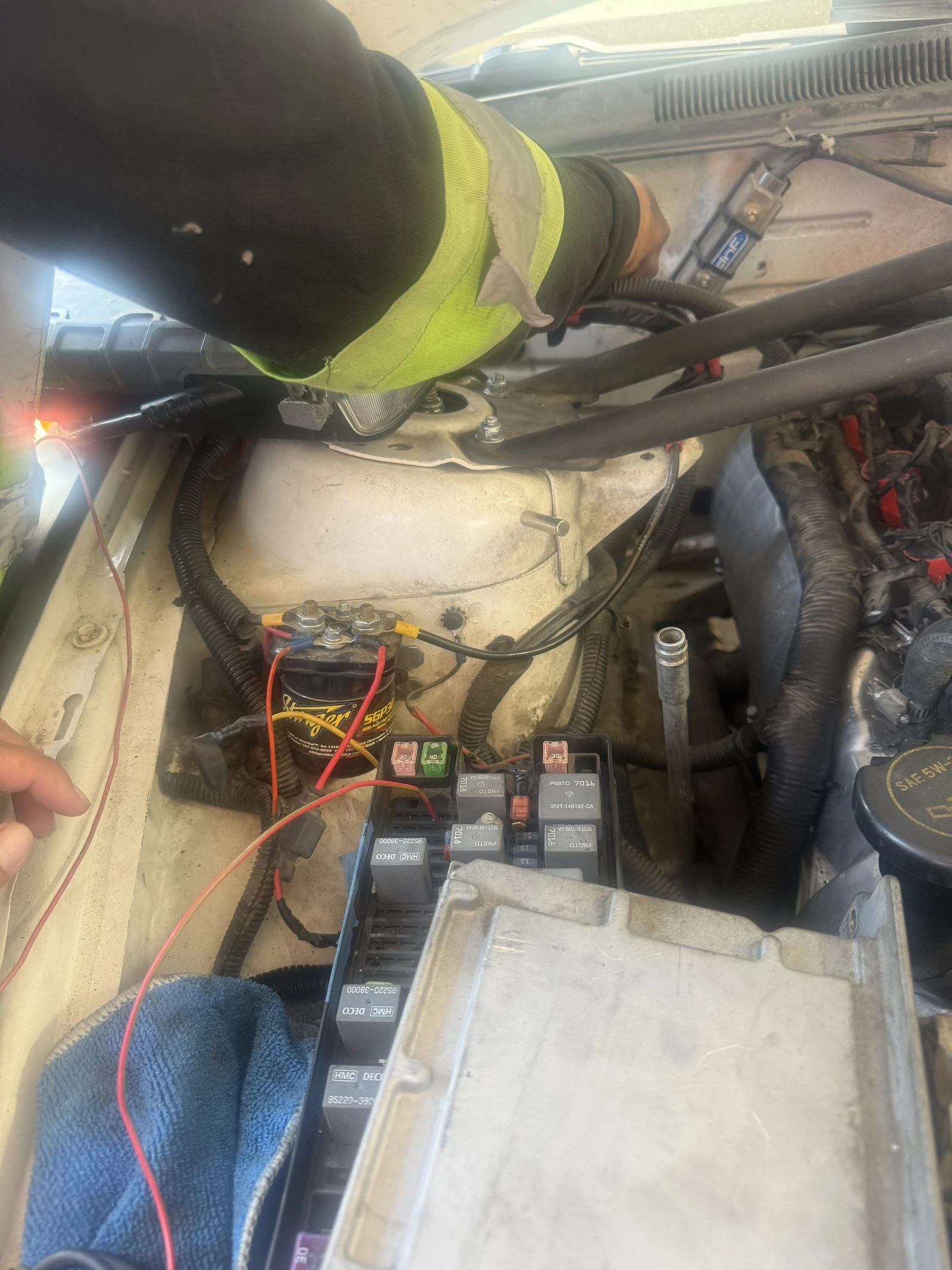 A Supercanic tech back probing a circuit at the fuse box under the hood, with test leads clipped on